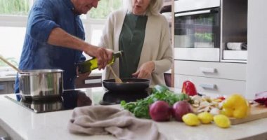Evde, mutfakta kıdemli beyaz bir çift, karısı tavada sebzeleri karıştırırken, adam yağ dökerken, yavaş çekimde konuşuyor. Coronavirus covid 19 karantina süresince birlikte iyi vakit geçireceğiz..