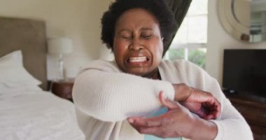 Dirseğine hapşıran Afrikalı Amerikalı son sınıf öğrencisi bir kadın. Evdeki yatakta otururken burnunu mendille siliyor. Koronavirüs salgını sırasında karantinaya alınma