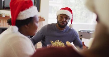Yemek masasında oturan Afro-Amerikalı adam konuşuyor. Noel 'de evde birlikte yemek yerken Noel Baba şapkası takmak. Noel bayramı geleneği kutlaması