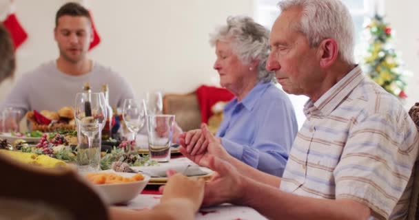 白人家庭正在享用圣诞大餐 圣诞节期间 他们手牵手坐在餐桌前 一起祈祷 然后在家里吃午饭 圣诞节庆祝活动的传统 — 图库视频影像