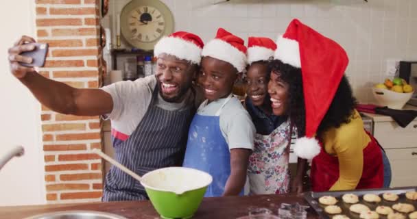 非洲裔美国人家庭在烘烤的时候带着智能手机自拍 在家里的圣诞期间 在厨房里戴着圣诞帽 圣诞节庆祝活动的传统 — 图库视频影像
