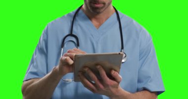 Yeşil ekranda beyaz erkek doktor var. Omuzlarına steteskop ve önlük takmış bir adam tablet bilgisayar kullanıyor..