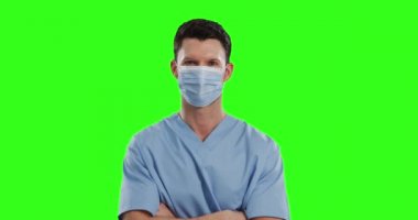 Beyaz erkek doktor yeşil ekran arka planında yüz maskesi takıyor. Önlük giymiş, kameraya bakan bir adamın portresi. Coronavirus covid 19 salgını sırasında tıp alanında hijyen..