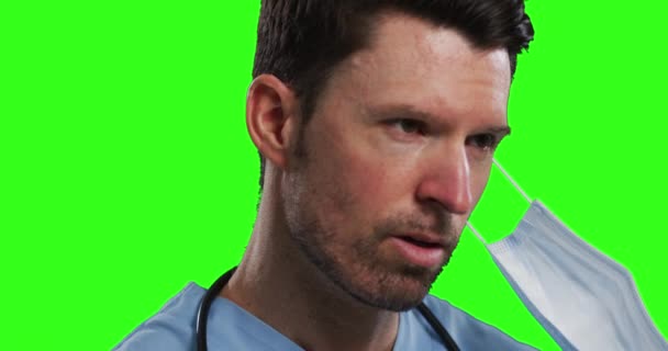 白种人男医生戴着面具在绿色屏风背景下 戴着洗涤剂摘下面具的男人 食管癌大流行期间医学专业的卫生情况 — 图库视频影像