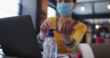 Modern ofiste el dezenfektanı kullanan yüzü maskeli beyaz bir kadın. Coronavirus covid 19 salgını sırasında işyerinde hijyen ve sosyal mesafeler.