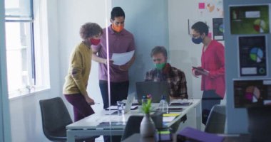 Modern ofisteki toplantı odasında yüz maskesi takan çeşitli meslektaşlar birlikte çalışıyor. Coronavirus covid 19 salgını sırasında işyerinde hijyen ve sosyal mesafeler.