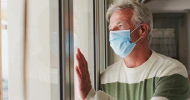 Yüz maskesi takan kıdemli beyaz adam evinden dışarı bakıyor.