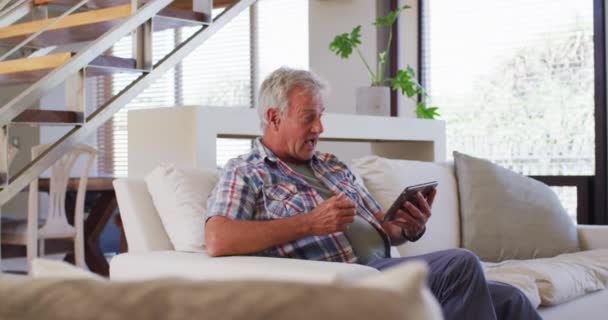 Старший кавказский мужчина, сидящий дома на диване в видеочате — стоковое видео