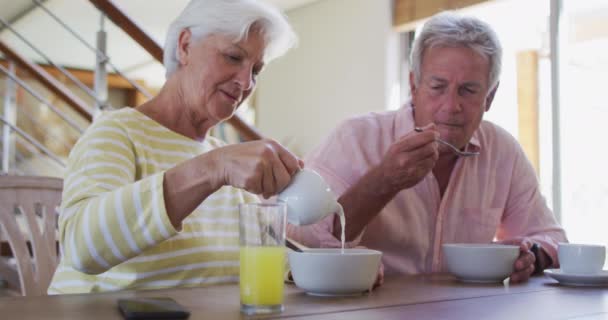 Senior kaukasischen Paar gießt Milch in Müslischale beim gemeinsamen Frühstück zu Hause — Stockvideo