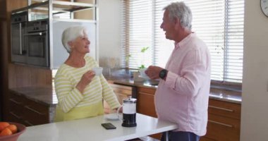 Üst düzey beyaz çift evdeki mutfakta kahve içerken birbirleriyle konuşuyorlar.
