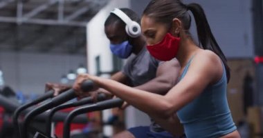 Yüz maskesi takan melez bir kadın spor salonunda egzersiz yapıyor. Çapraz antrenör makinesiyle çalışıyor. Coronavirus covid 19 salgını sırasında spor salonunda egzersiz yapıyor..