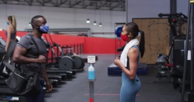 Formda Afro-Amerikan erkek ve beyaz kadın spor salonunda dirseklerine dokunarak yüz maskesi takıp birbirlerini selamlıyorlar. Koronavirüs salgını sırasında karantinaya alınma