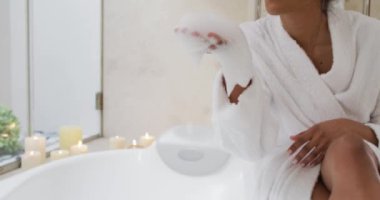 Karışık ırktan bir kadın küvetin yanında oturuyor.