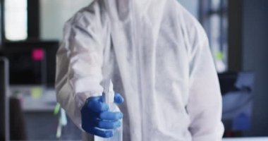 Koruyucu giysiler ve maske takan sağlık çalışanları modern ofiste dezenfektan sıkarlar. temizlik ve dezenfeksiyon önleme ve covid-19 salgınının kontrolü