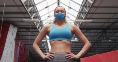 Spor salonunda elleri kalçasında duran, yüz maskesi takan beyaz bir kadın. Koronavirüs salgını sırasında karantinaya alınma