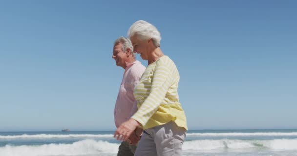 Boldog idős fehér pár kéz a kézben beszélgetnek, miközben sétálnak a parton. — Stock videók