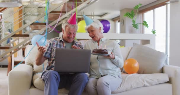 Üst düzey Kafkasyalı çift ellerinde pasta tutuyorlar ve doğum gününü kutluyorlar. Evde bilgisayarlarında görüntülü sohbet yapıyorlar. — Stok video