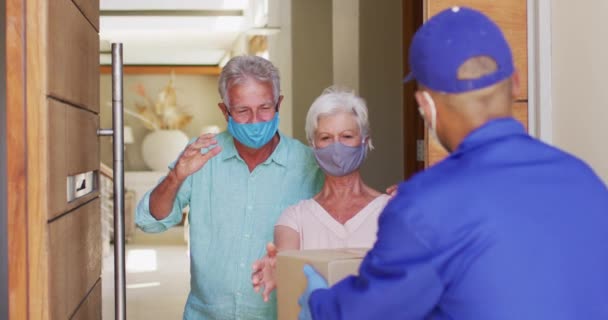 Consegna uomo consegna pacchetto per anziani coppia caucasica indossare maschere facciali a casa — Video Stock