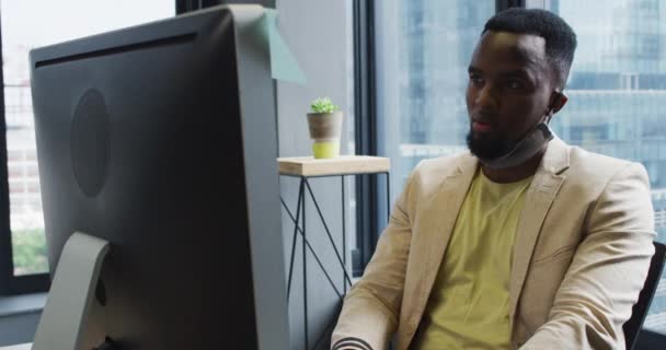 Afrykański Amerykanin Maską Szyi Korzystający Komputera Siedząc Biurku Nowoczesnym Biurze — Wideo stockowe