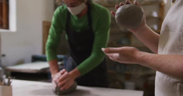 男女陶工戴着面罩和围裙 跪在陶瓷工作室的粘土 大肠病毒大流行期间陶器工作室的卫生与社会疏离D — 图库视频影像