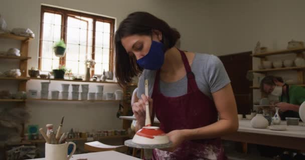 在陶瓷工作室 女性高加索陶工戴着面具 用釉刷在陶瓷轮上油漆壶 哥罗那未斯海盗时期陶器工作室的卫生与社会疏离19 — 图库视频影像
