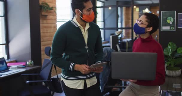 現代のオフィスで議論するラップトップのデジタルタブレットを使用して顔マスクを身に着けている多様な男性と女性の同僚 コロナウイルスの職場での衛生と社会的距離は19のパンデミックを克服しました — ストック動画