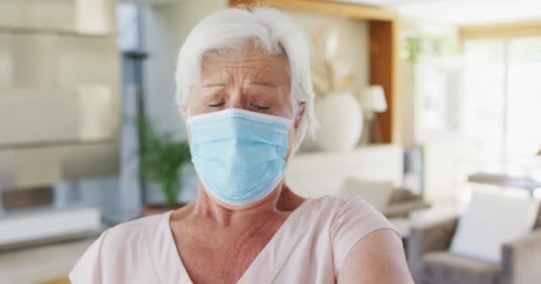 Старшая белая женщина в маске для лица чихает на локоть дома — стоковое видео