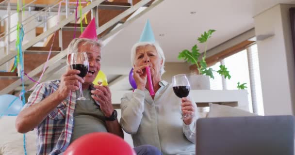 Senior kaukasischen Paar bläst Party-Gebläse feiern Geburtstag Toasten Weingläser zu Hause — Stockvideo