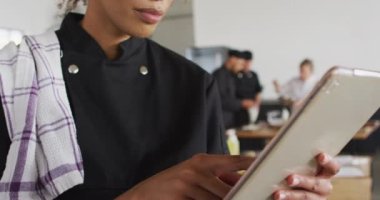 Dijital tablet kullanan karışık ırk aşçısı. Yemek hazırlamak ve gülümsemek. Profesyonel bir mutfakta çalışıyorum..