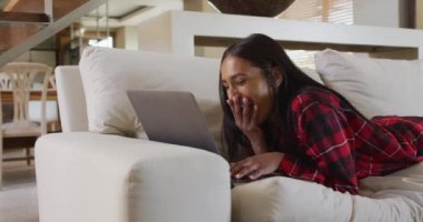 Evdeki koltukta video sohbeti yapan karışık ırklı bir kadın.