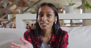 Evdeki koltukta video sohbeti yapan karışık ırklı bir kadın.