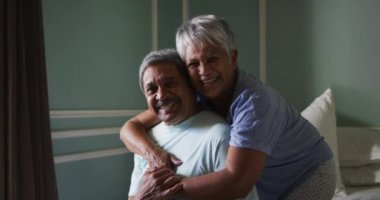 Üst düzey melez çift yatak odasında sarılıp gülüyor.