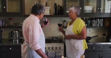 Son sınıf melez çift şarap içip mutfakta yemek hazırlıyor.