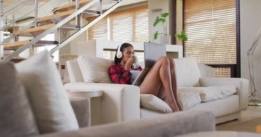 Evdeki kanepede müzik dinleyen karışık ırklı bir kadın.