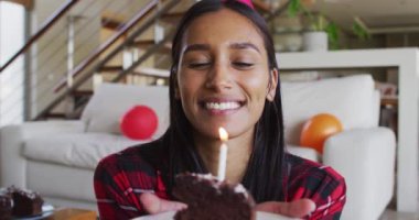 Karışık ırk kadını dizüstü bilgisayar kullanıyor, elinde mum üfleyen bir pasta tutuyor.