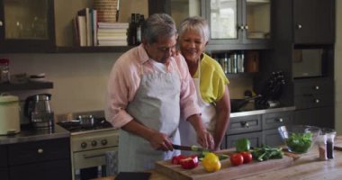Önlük giyip mutfakta yemek hazırlayan mutlu son sınıf melez çift.