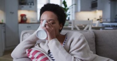 Kanepede oturup kahve içen melez bir kadın.