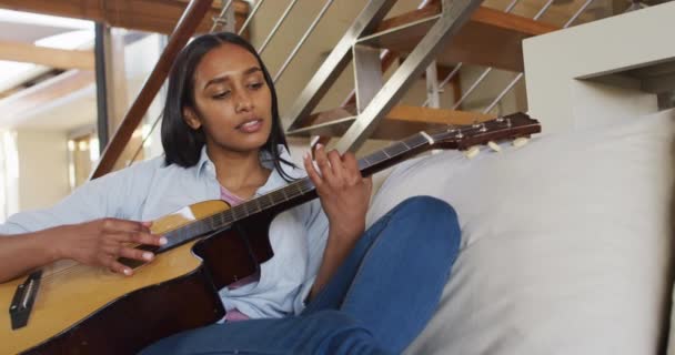 Donna razza mista sul divano a casa a suonare la chitarra e cantare — Video Stock