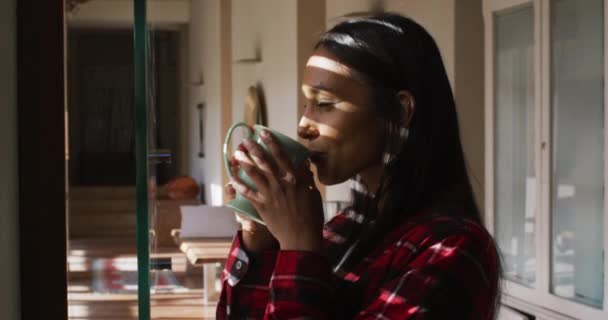 Vegyes rasszista nő áll az ablakban otthon kávézás — Stock videók
