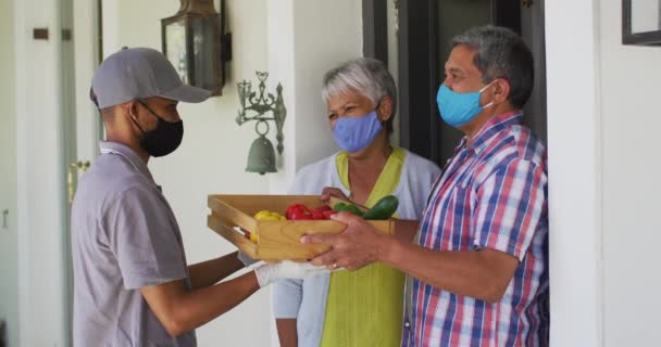 Sénior misto casal de raça e entrega de alimentos homem na porta usando máscaras faciais — Vídeo de Stock