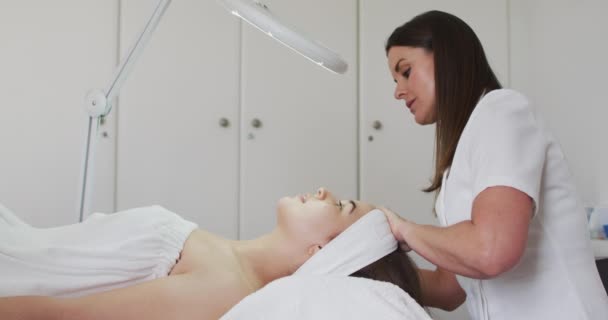 Caucásica mujer recostada mientras esteticista le da un facial — Vídeos de Stock