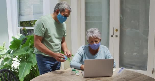 안면 마스크를 착용하고 노트북으로 진료를 받고 있는 고위 인종 커플 — 비디오
