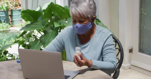 Mulher de raça mista sênior usando máscara facial tendo consulta médica usando laptop — Vídeo de Stock