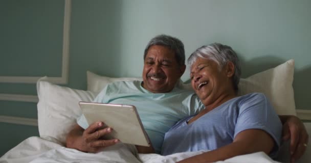 Šťastný senior smíšené rasy pár sedí v posteli pomocí tabletu — Stock video
