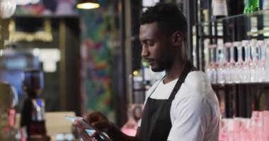 Afro-Amerikan kahveci kafede gülümseyen tablet kullanıyor.