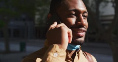 Yüzü maskeli Afro-Amerikan işadamı akıllı telefondan konuşuyor.