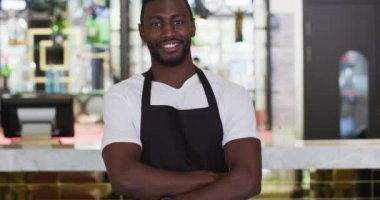 Kafede önlük giymiş kameraya gülümseyen Afrikalı Amerikalı baristanın portresi.