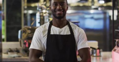 Kafede önlük giymiş kameraya gülümseyen Afrikalı Amerikalı baristanın portresi.