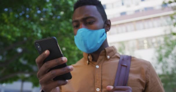 Empresario afroamericano con máscara facial usando smartphone en la calle — Vídeos de Stock