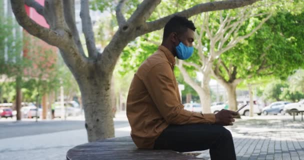 Homme d'affaires afro-américain portant un masque facial en utilisant une tablette assise sur un banc — Video